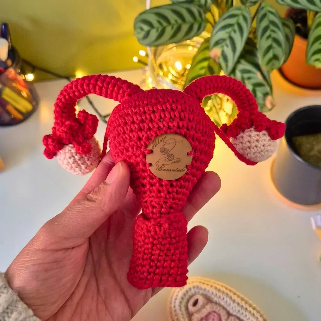 Hand holding a crocheted uterus model in a cozy setting with plants