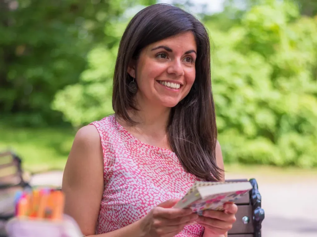 Carmen smiling while holding notes in a park setting